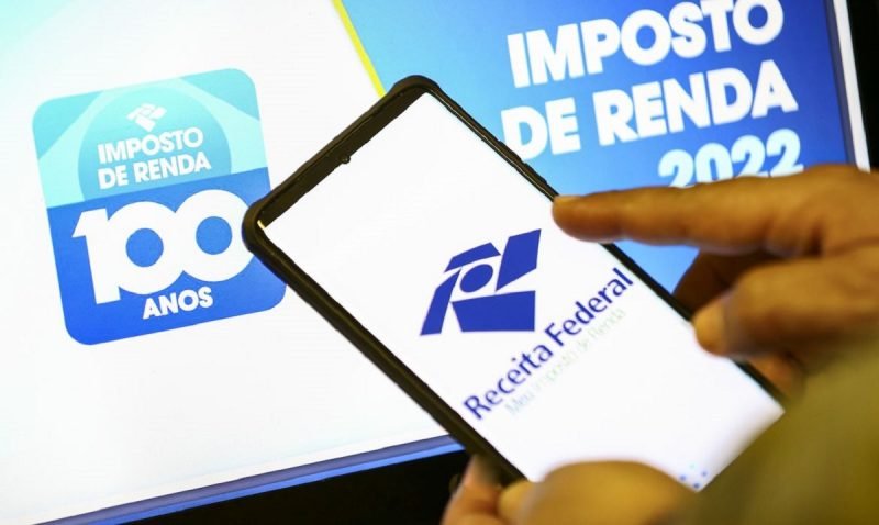 Foto mostra pessoa segurando um celular e entrando no site da receita federal para declarar o seu imposto de renda